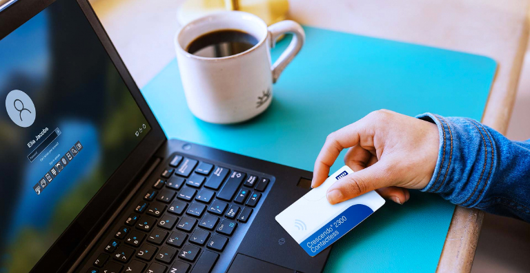A person holding a smart card next to a laptop and a cup of coffee.