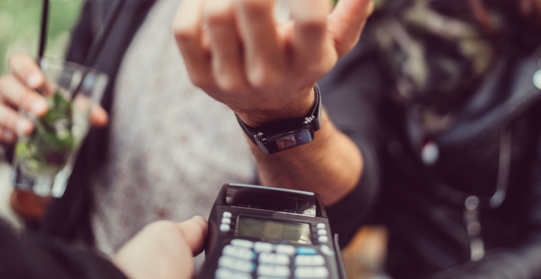 Persona usando un reloj inteligente para pagar una factura.