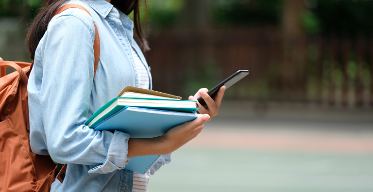 student holding books and phone
